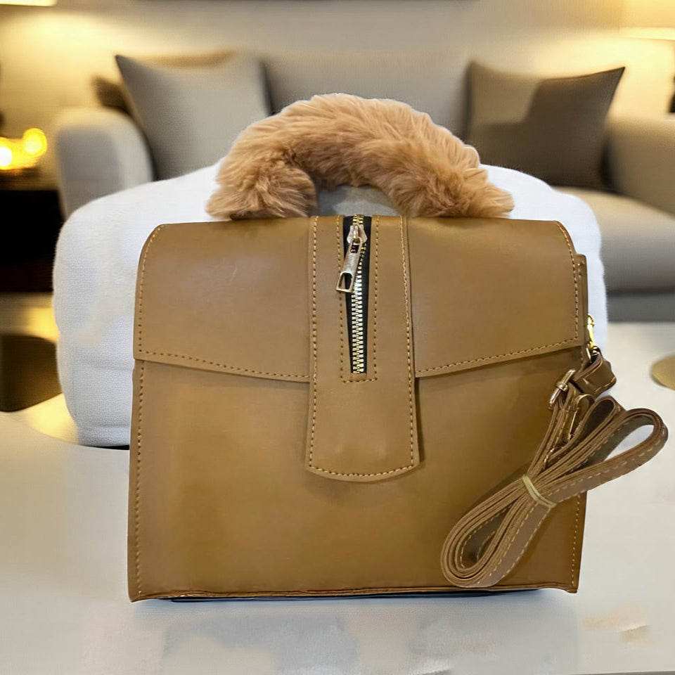 Tan leather handbag with fur trim on a white surface, blurred indoor background